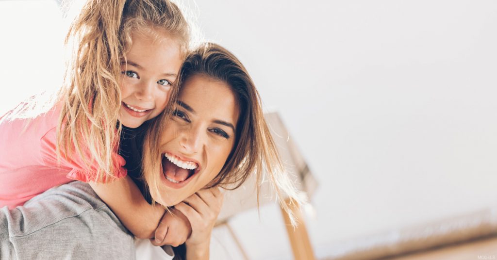 Young girl hugging mother around the neck as both laugh