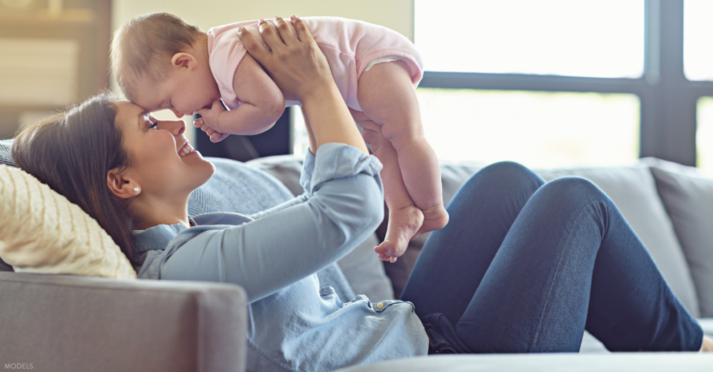 Mom sitting on couch lifting baby.