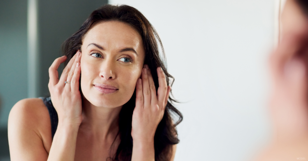 Woman holding hair back as she looks at herself in a mirror