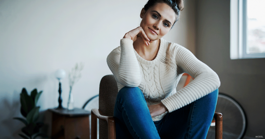 Woman in jeans and sweater sitting and smiling at camera with cocked head