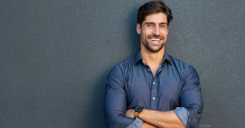 Attractive man leaning against a wall with his arms crossed and smiling (model)